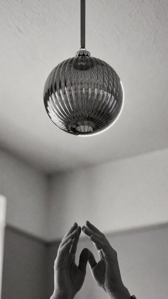 Ornamento de Natal em vidro cinzento pendurado com textura estriada e mãos ao fundo