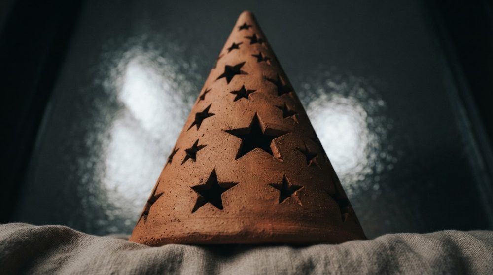 Lanterna de barro castanho em forma de cone com estrelas recortadas sobre tecido neutro