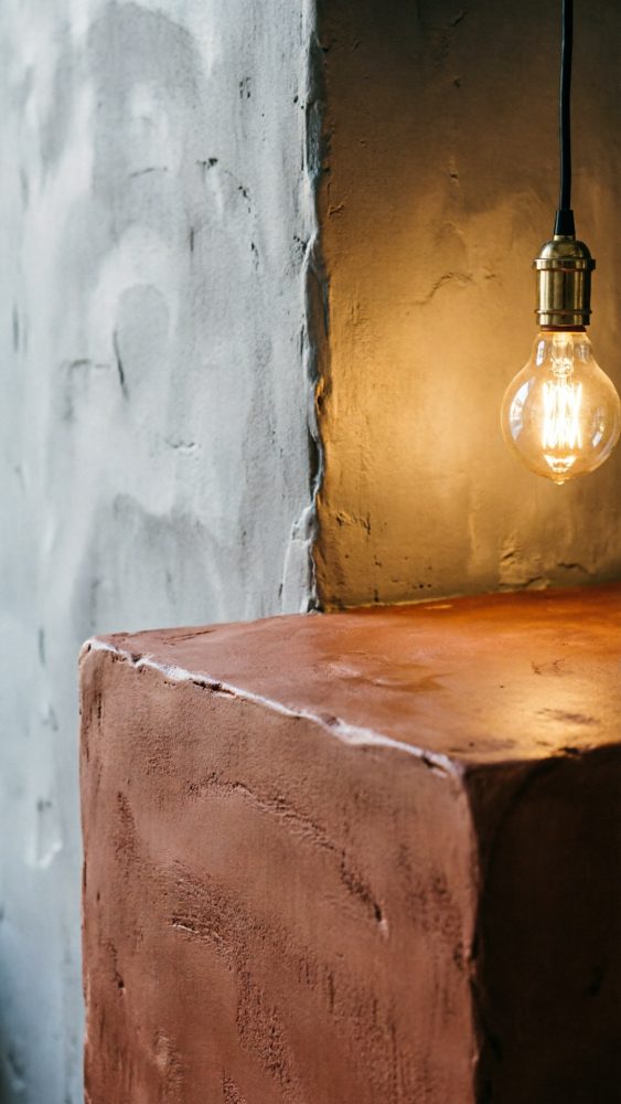 Superfície rústica castanha com parede cinzenta texturada e lâmpada pendente iluminada