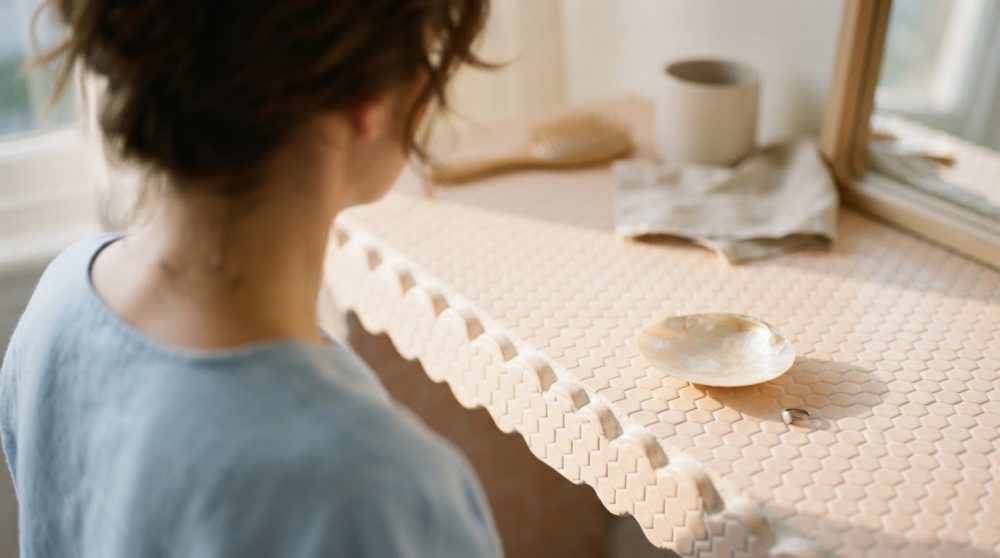 Pessoa de costas olhando para superfície de azulejos bege com borda ondulada e objetos pequenos
