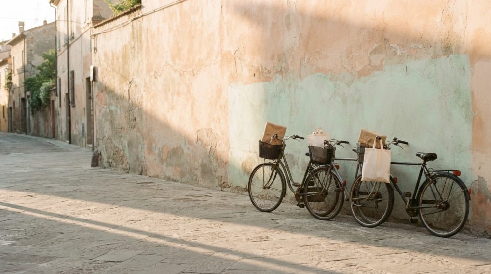 Duas bicicletas com cestos e sacos encostadas a parede de rua antiga de pedra em luz natural