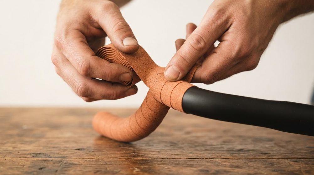 Punho de guiador com fita de cortiça a ser enrolada por mãos masculinas numa mesa de madeira