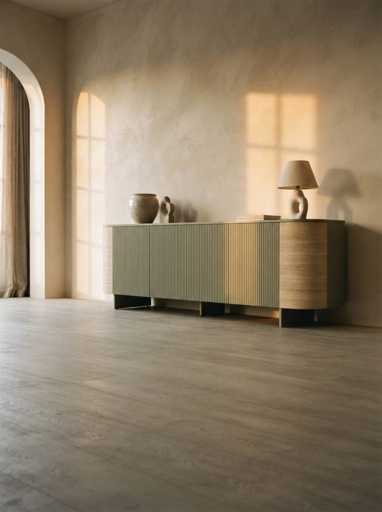 Aparador moderno em madeira clara com vaso, escultura e candeeiro num ambiente minimalista com luz natural