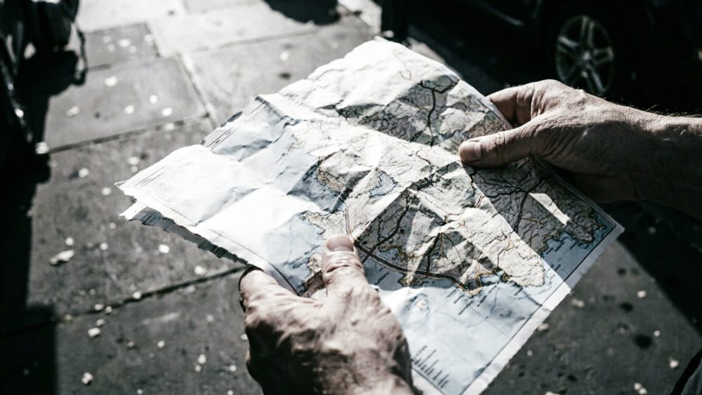 Mãos de pessoa sénior segurando mapa de papel vincado ao ar livre em cidade