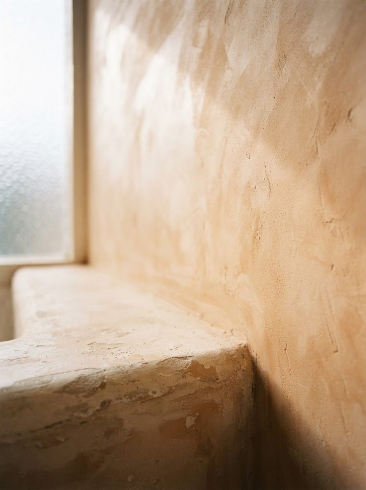 Parede e superfície rústica com textura em tons terrosos iluminada por luz suave de janela fosca