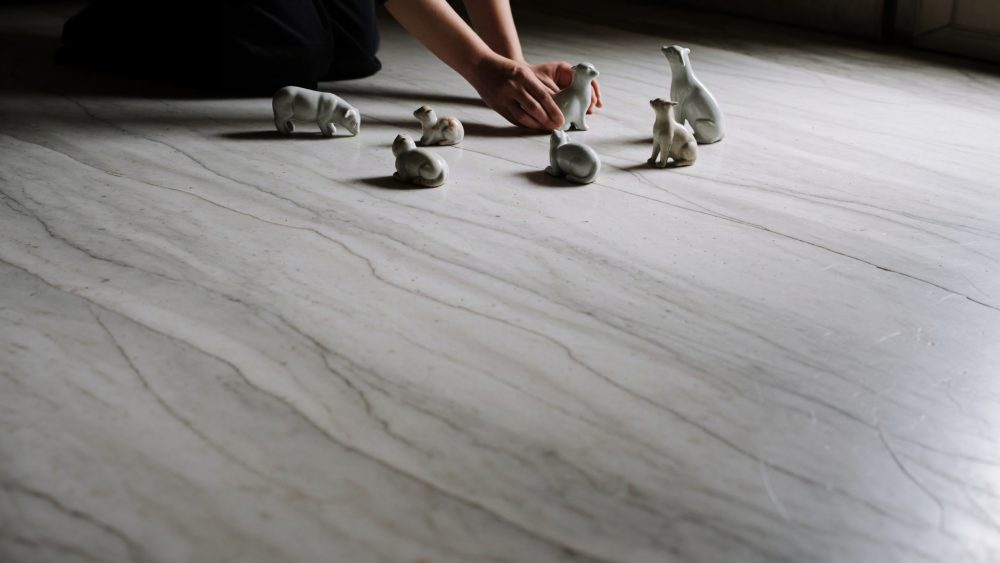 Mão a organizar pequenos objetos em porcelana branca sobre chão de mármore cinzento
