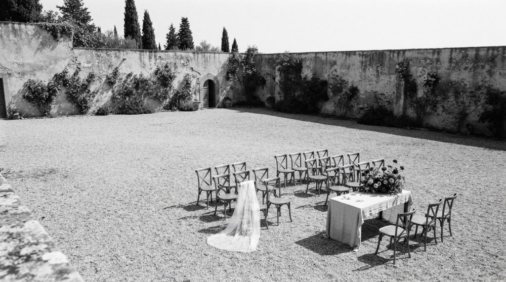 Espaço exterior para cerimónia de casamento com cadeiras, mesa com flores e véu de noiva ao sol