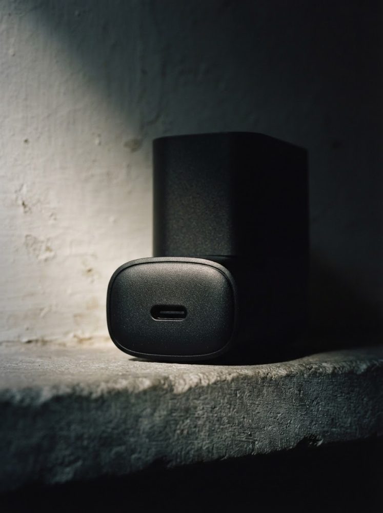 Carregador USB-C preto compacto sobre superfície de cimento escurecida