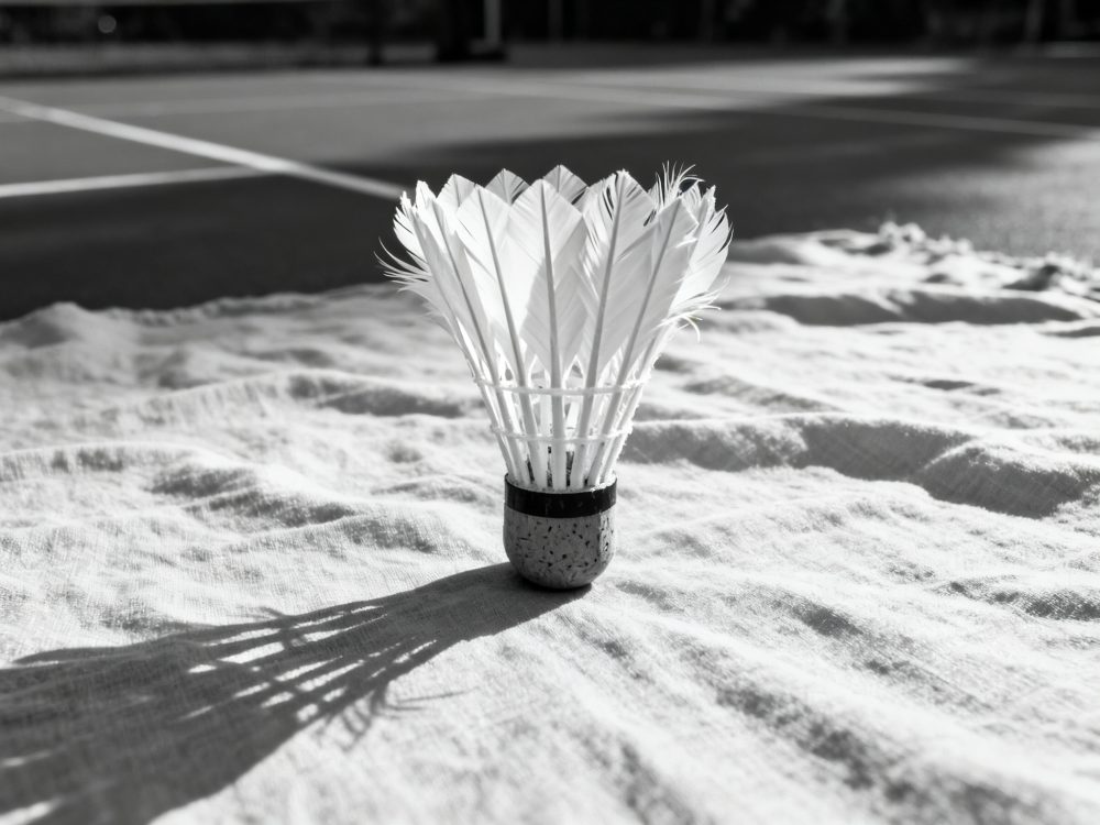 Volante de badminton branco em cima de tecido com sombras em fundo de campo de desporto