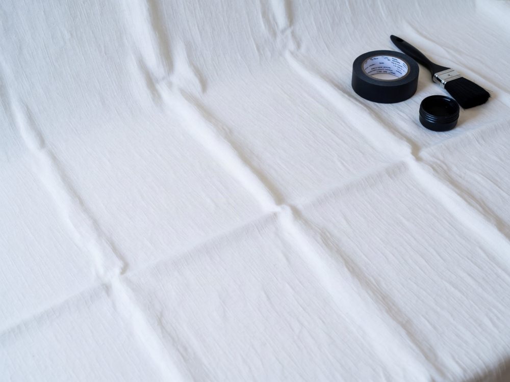Superfície de tecido branco com pincel, tinta preta e fita adesiva preta no canto