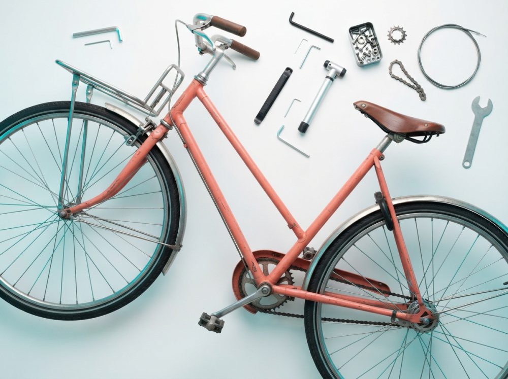 Bicicleta cor-de-rosa com ferramentas para manutenção dispostas em fundo branco