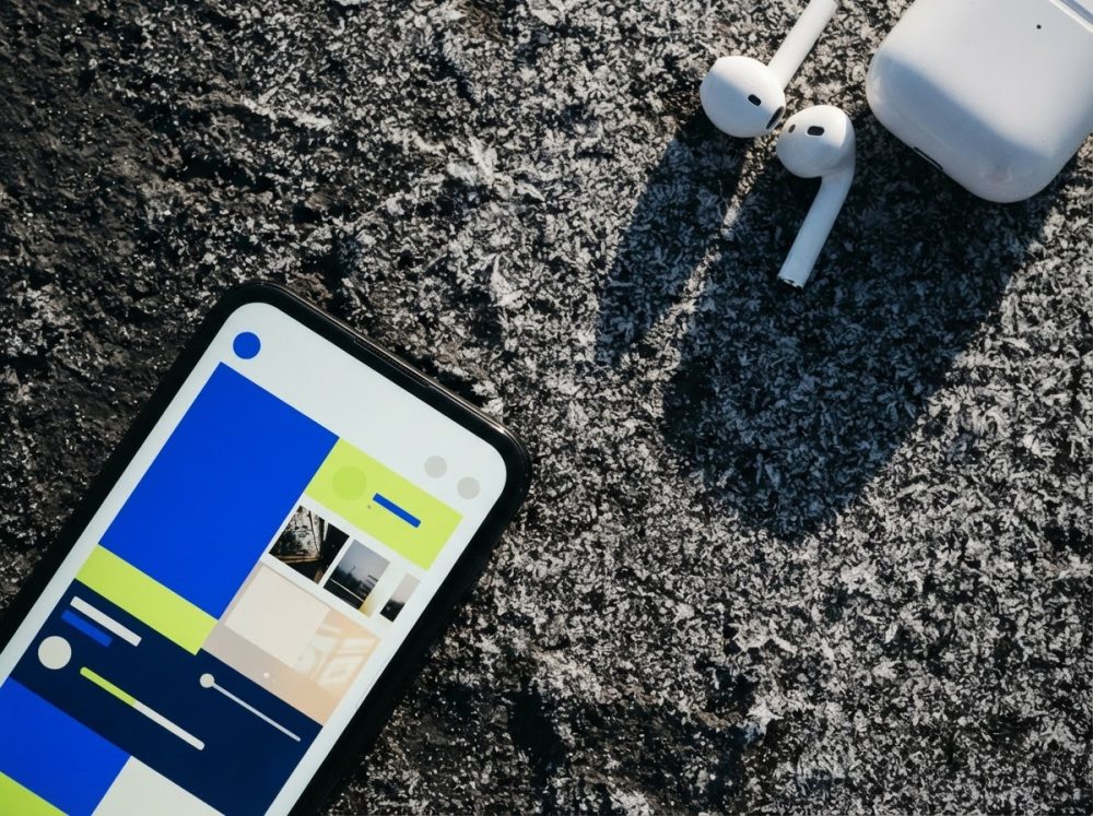 Smartphone com ecrã colorido e auscultadores sem fios brancos num fundo asfáltico escuro