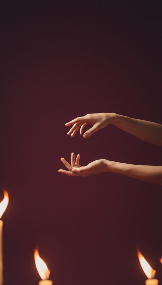 Mãos em pose delicada sobre velas acesas com fundo escuro