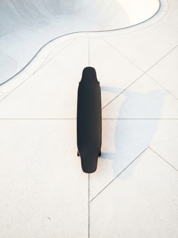 Skateboard preto visto de cima num piso branco com linhas geométricas num parque de skate