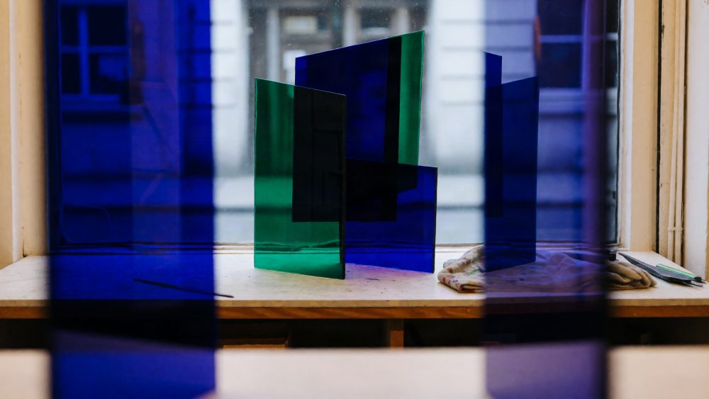 Painéis abstratos verticais de vidro azul e verde numa mesa junto a janela