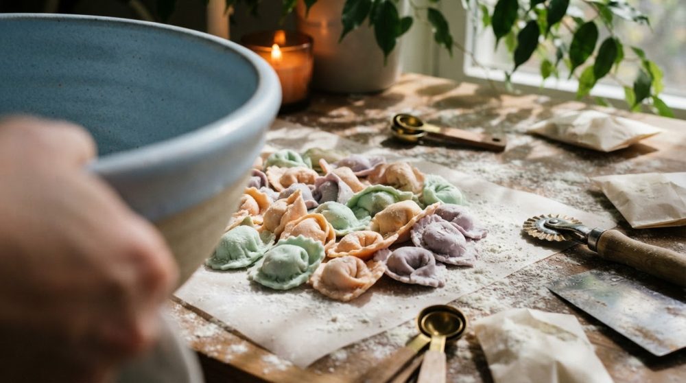 Massa colorida caseira de raviolis sobre mesa de madeira com utensílios de cozinha
