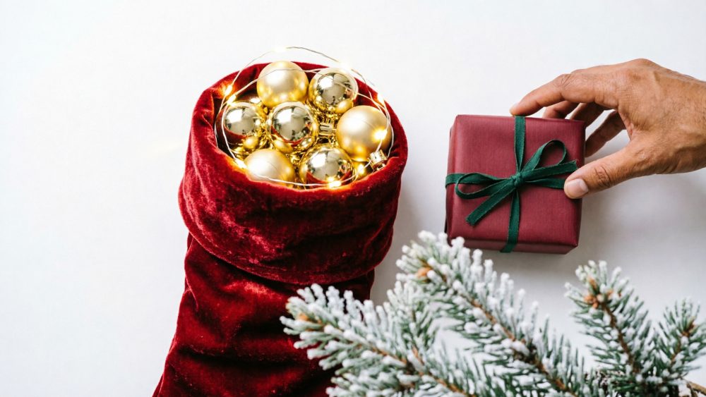Bota de Natal vermelha com bolas douradas, presente vermelho com fita verde e ramos de pinheiro nevados
