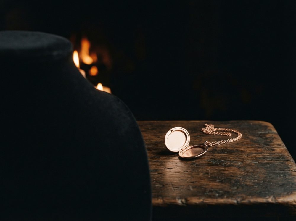 Colar dourado com medalhão aberto sobre mesa rústica e fundo escuro com luz quente