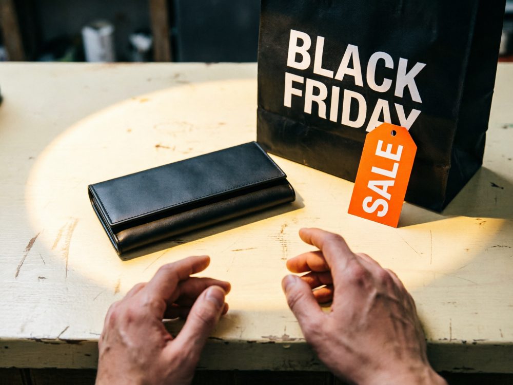 Carteira preta sobre mesa junto a saco Black Friday com etiqueta de desconto vermelha e mãos próximas