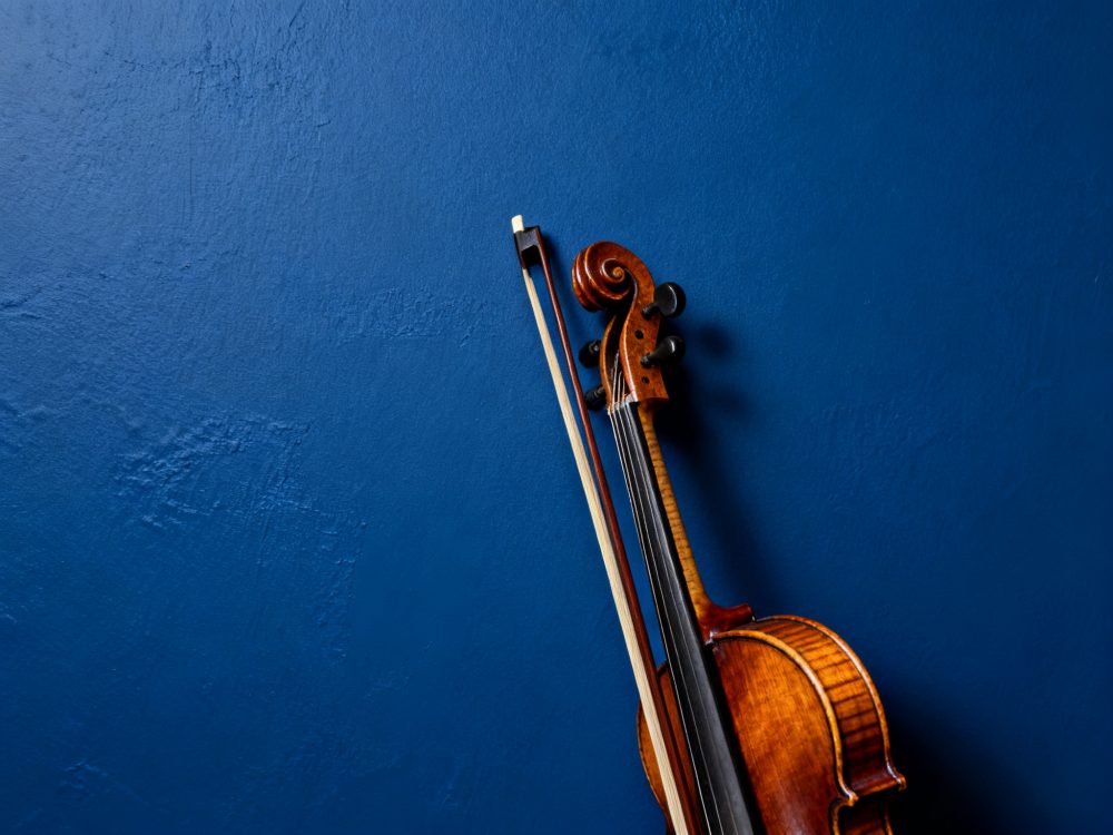 Violino de madeira com arco apoiado numa parede azul escura