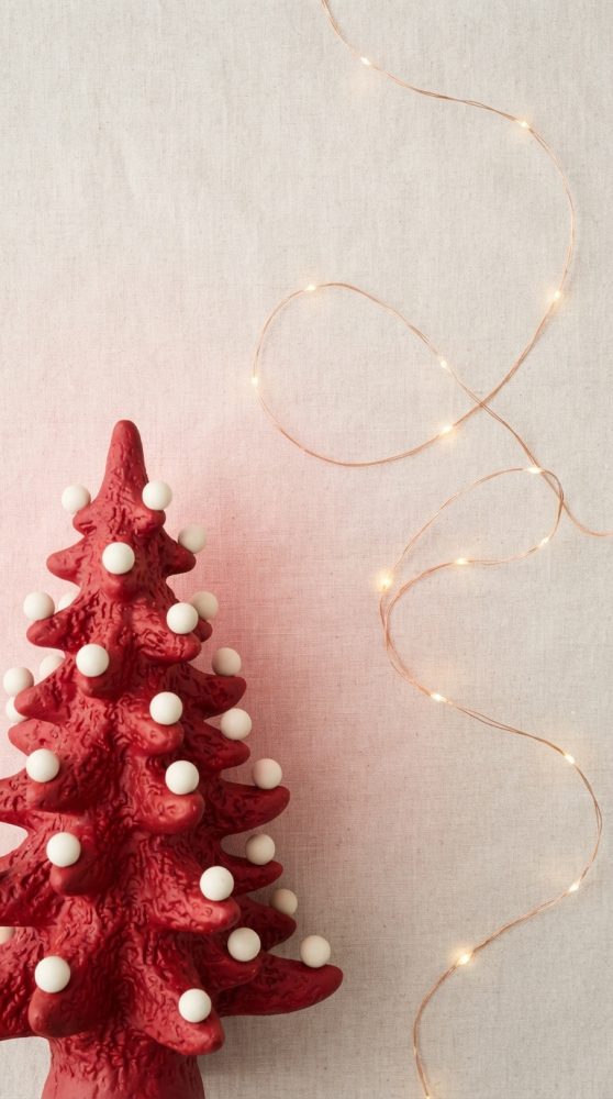 Árvore de Natal vermelha com bolas brancas e luzes de fada douradas sobre fundo bege