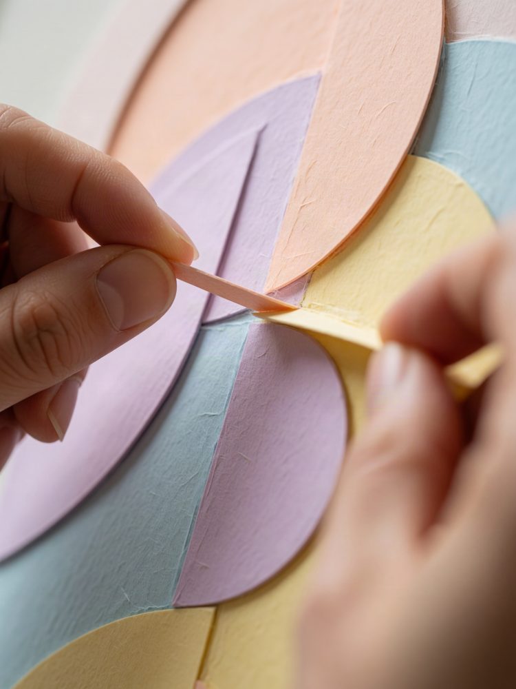 Mãos a montar formas circulares de papel colorido em tons pastel em arte abstrata