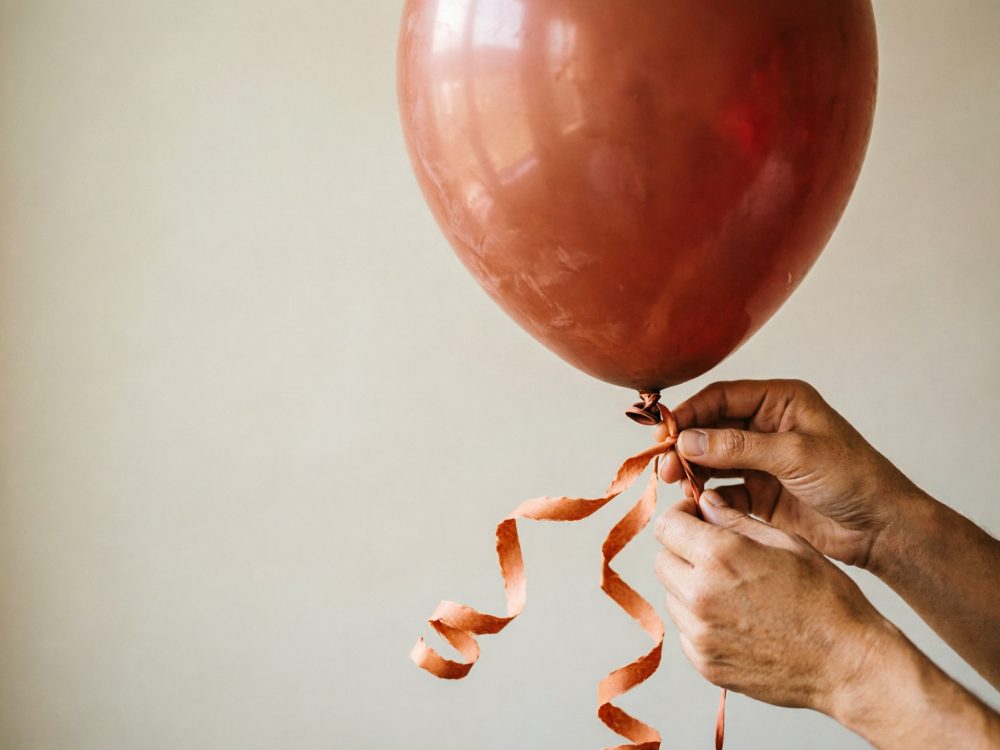Mãos a segurar um balão metálico laranja com fita enrolada pendurada