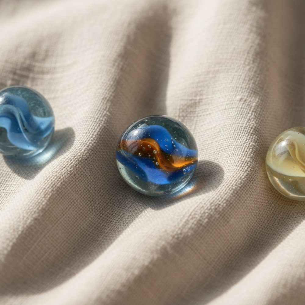 Três bolas de gude coloridas sobre tecido bege com textura e luz natural
