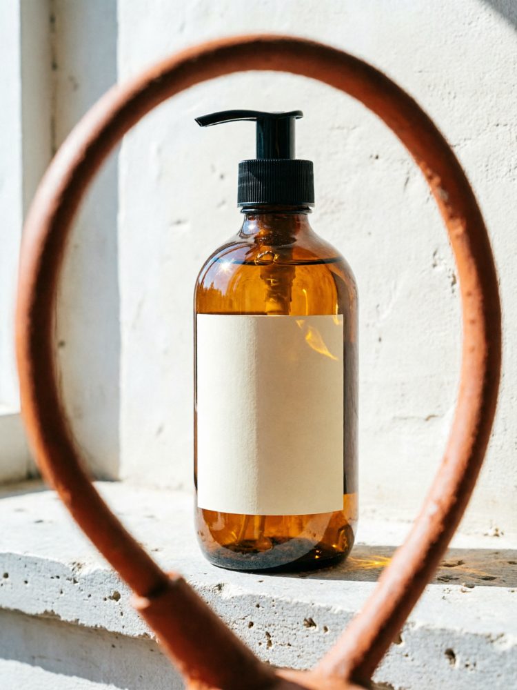 Frasco âmbar com dispensador preto e rótulo branco numa superfície iluminada natural