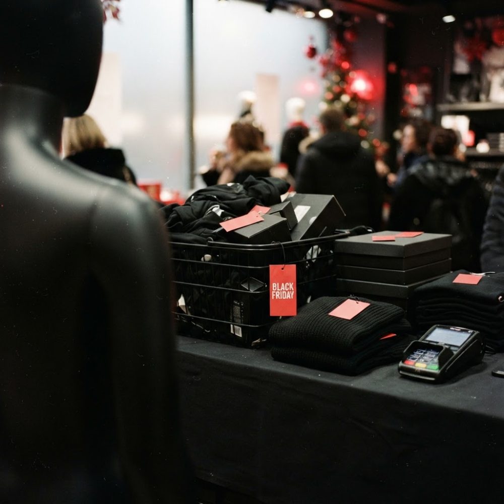 Mesa numa loja com roupas e caixas etiquetadas com Black Friday e clientes ao fundo