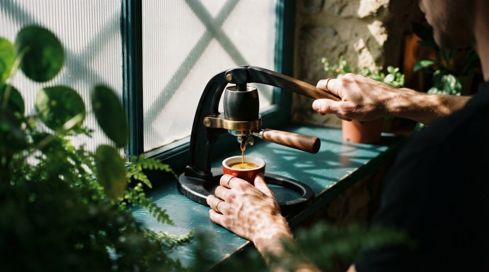 Pessoa a usar máquina de café manual para preparar expresso junto à janela com plantas e luz natural