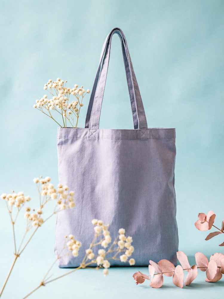 Saco de lona cinzento com ramos de flores secas em fundo azul claro