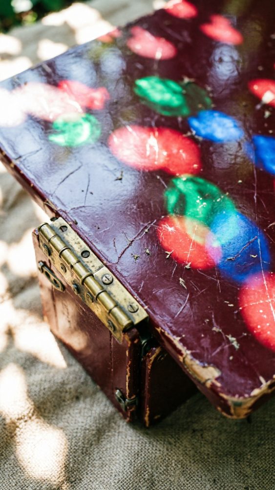 Mesa vintage bordô envelhecida com dobradiça metálica e reflexos coloridos na superfície