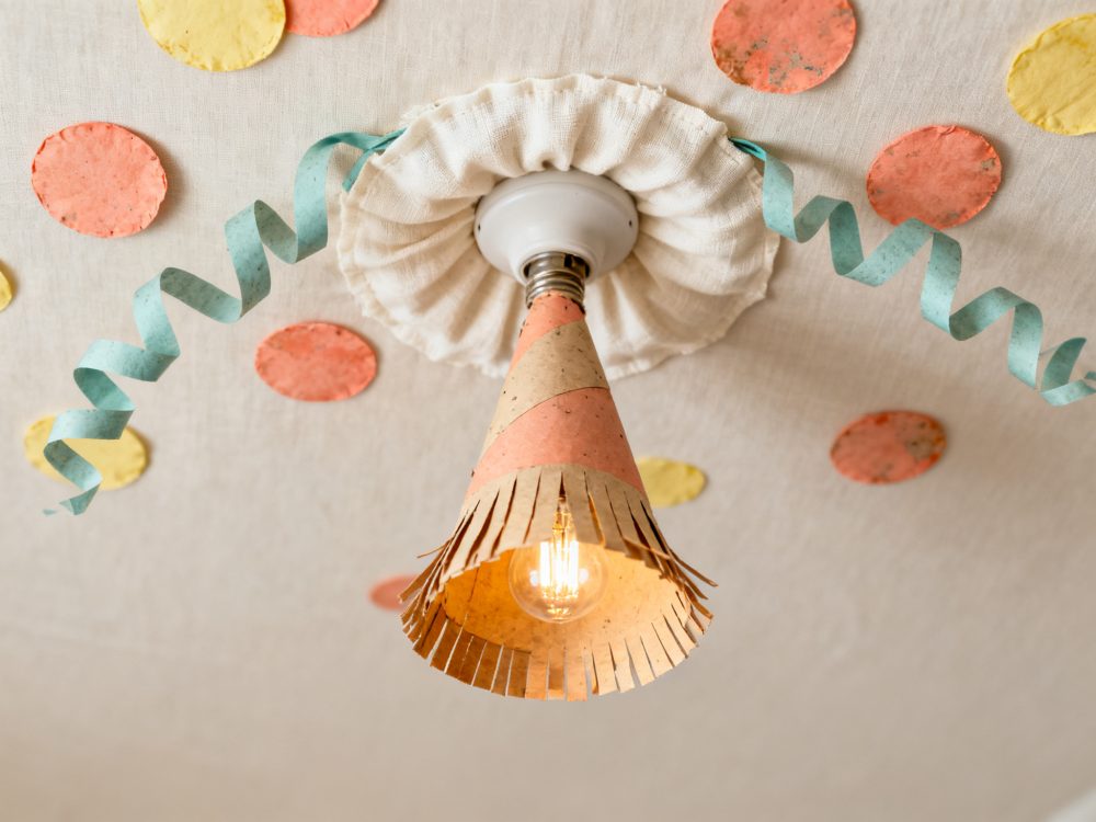 Luz de teto com abajur de papel, serpentinas azuis e confetes amarelos e cor-de-rosa no teto