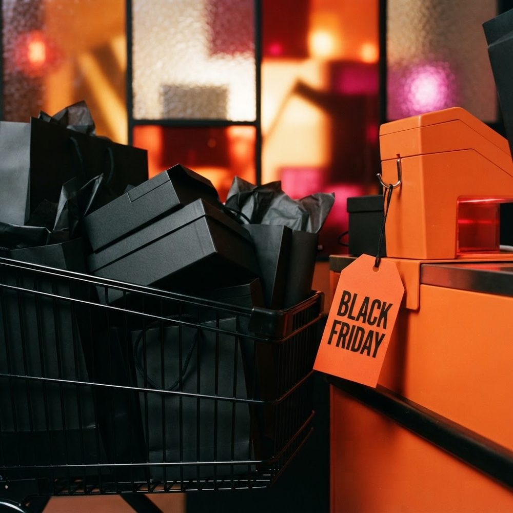 Carrinho com sacos e caixas negras junto a caixa registadora laranja com etiqueta Black Friday