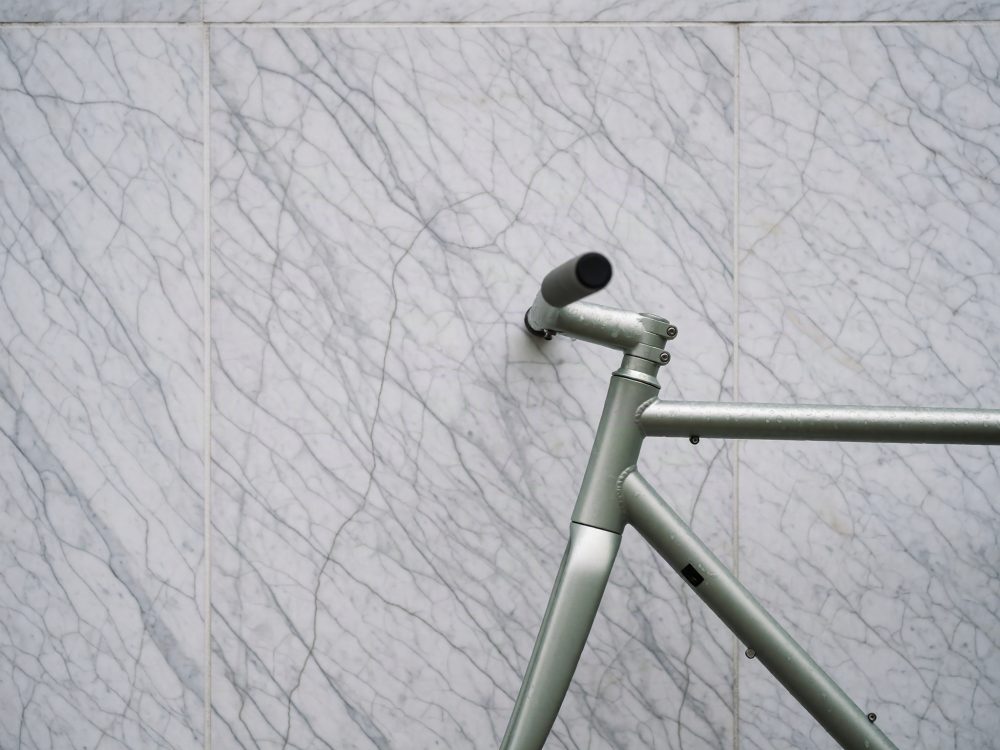 Parte da frente de quadro cinzento de bicicleta contra parede branca de mármore