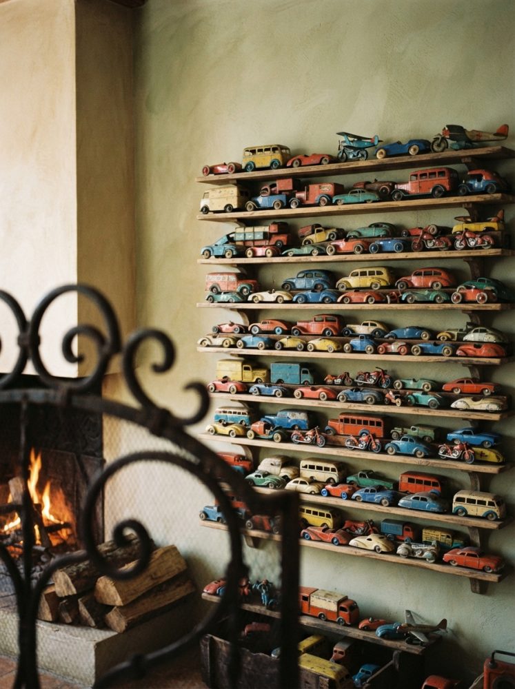 Miniaturas de carros e aviões vintage em prateleiras de madeira com lareira acesa ao lado
