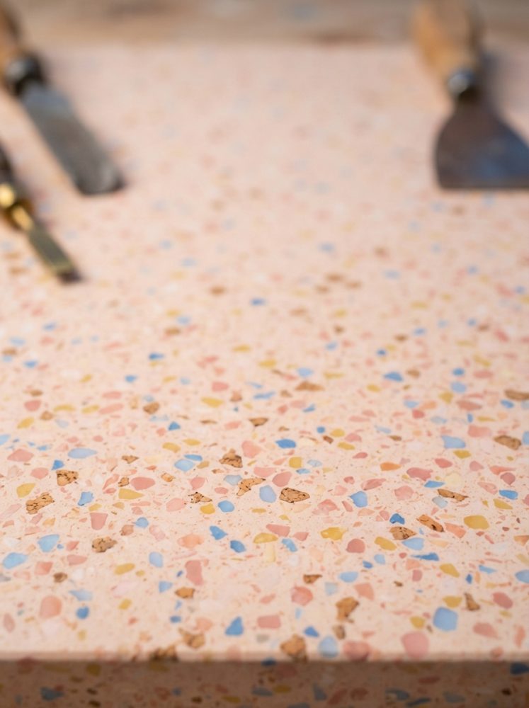 Superfície de terrazzo colorido com fragmentos em rosa, azul e amarelo e ferramentas desfocadas ao fundo