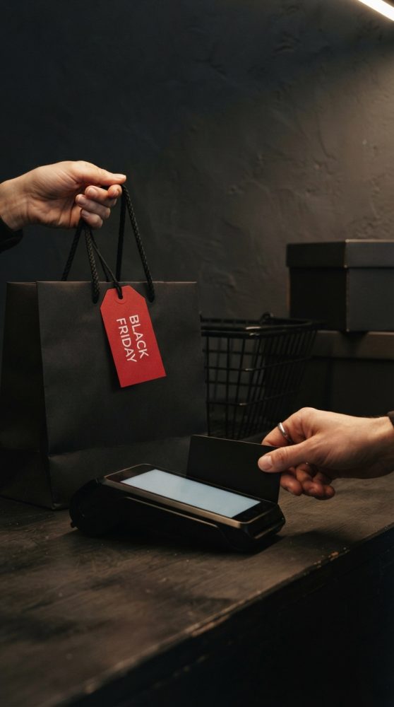 Mãos com saco de compras Black Friday e pagamento contactless por cartão num terminal pos