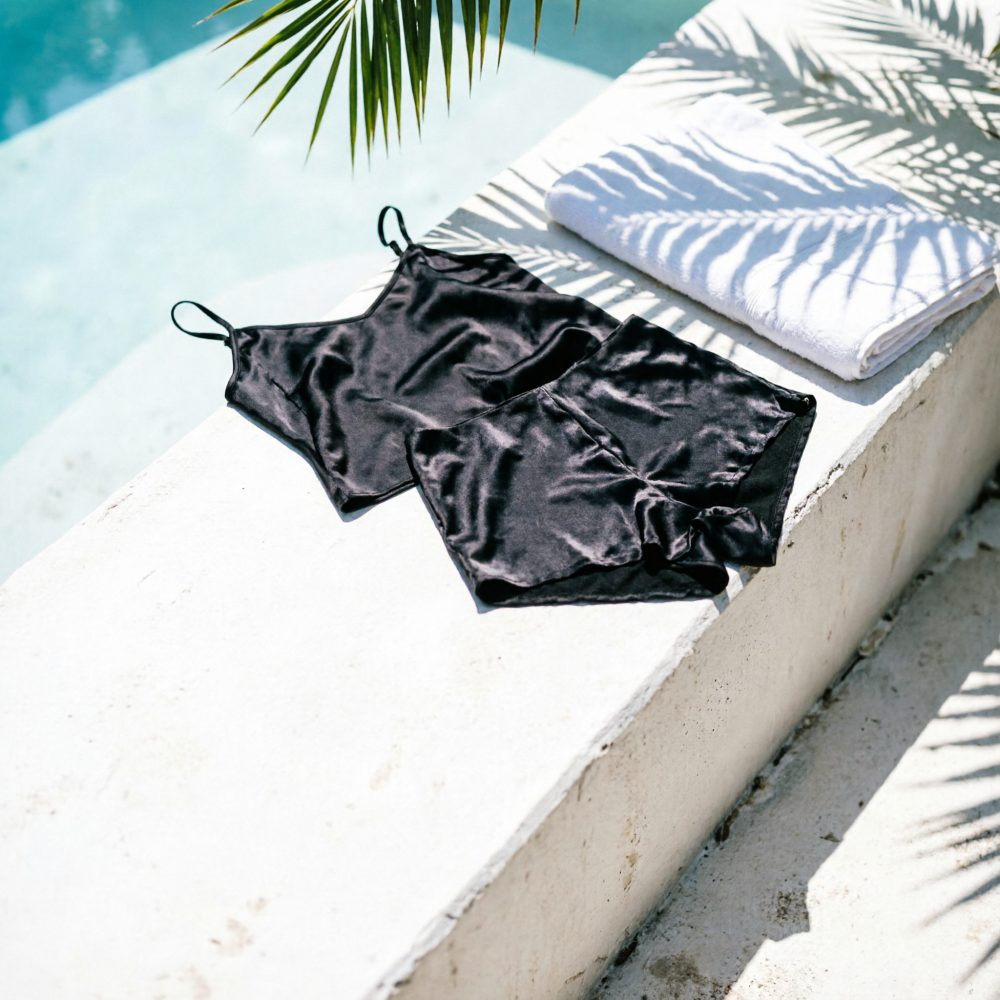 Conjunto preto de lingerie em cetim com top de alças e calções sobre superfície branca ao ar livre