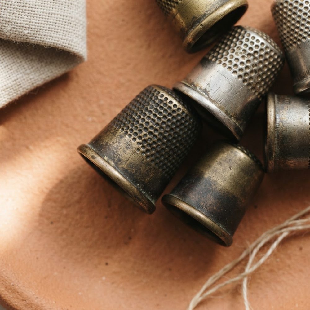 Conjunto de dedais metálicos antigos com desgaste sobre prato castanho claro