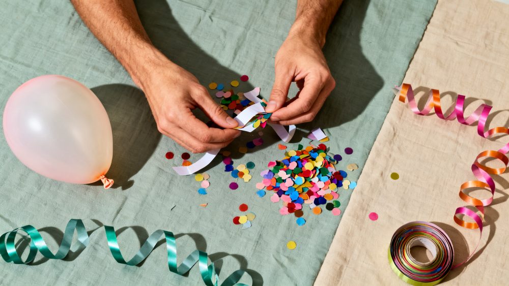 Mãos manuseando confetis coloridos com balão e serpentinas sobre tecidos claros