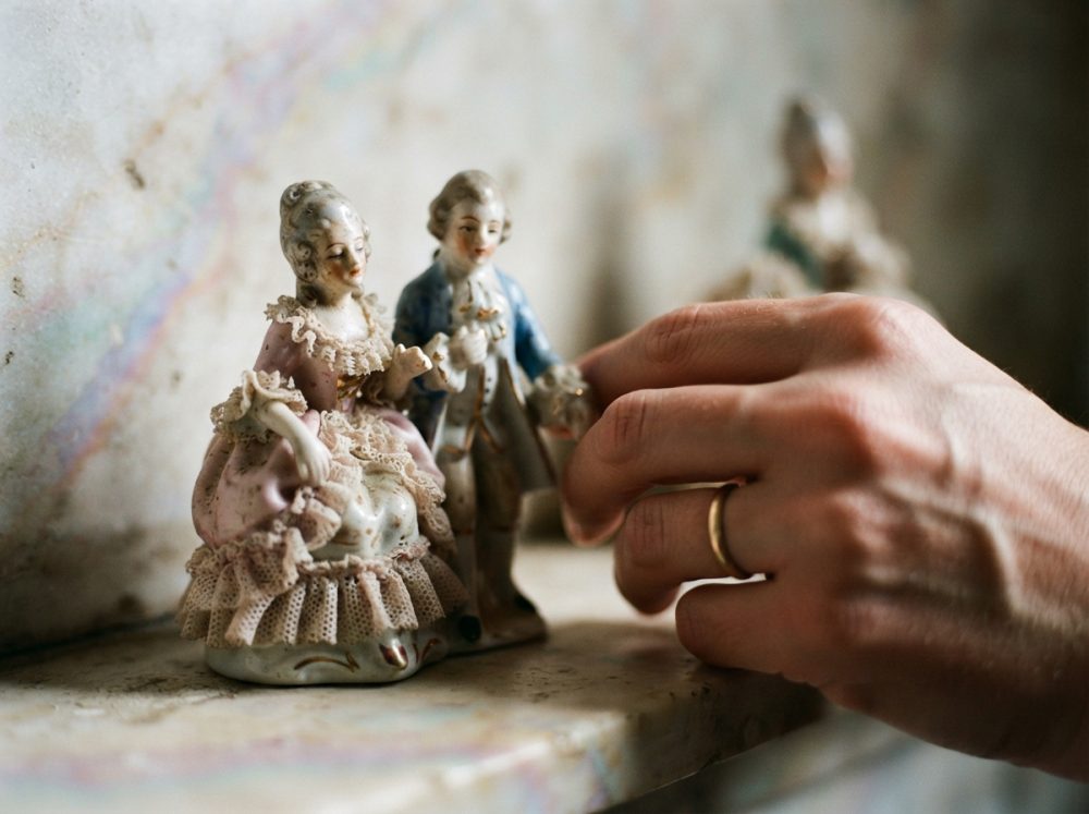 Mão humana segura figura de porcelana antiga de casal em trajes clássicos sobre superfície de mármore