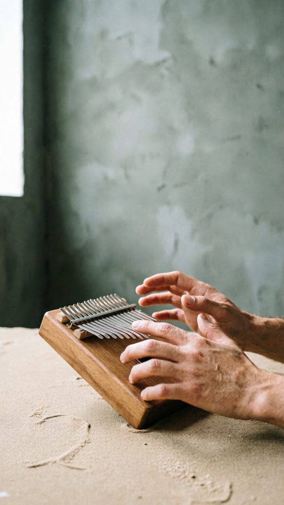 Mãos a tocar um instrumento musical kalimba de madeira com teclas metálicas