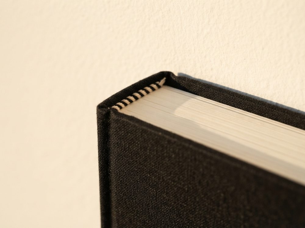 Canto superior de livro com capa preta e páginas creme numa iluminação suave