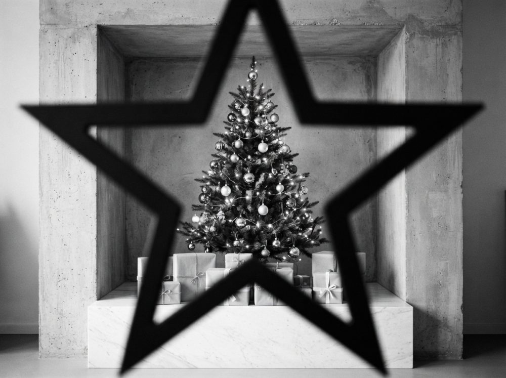 Árvore de Natal decorada com bolas e luzes com presentes e a silhueta de uma estrela preta em primeiro plano