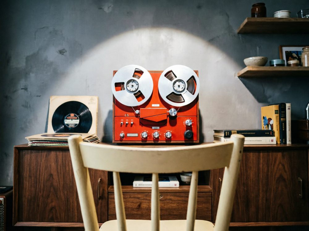 Aparelho de fita vintage vermelho com vinis e livros numa mesa de madeira contra parede cinzenta