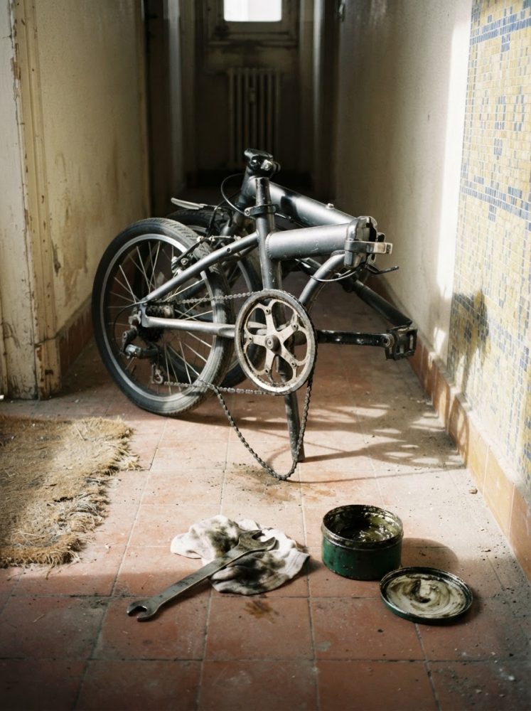 Bicicleta desmontada num corredor com chave inglesa, pano e massa lubrificante no chão