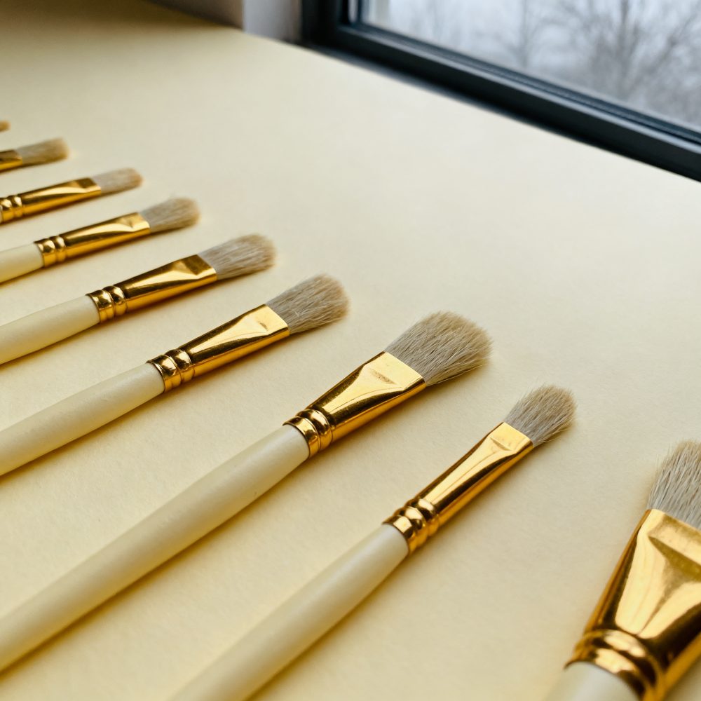 Pincéis de pintura alinhados diagonalmente sobre fundo amarelo próximo a janela