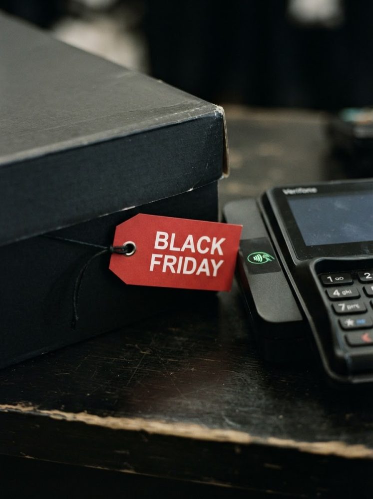 Caixa preta com etiqueta vermelha Black Friday e leitor de cartão ao lado em mesa escura
